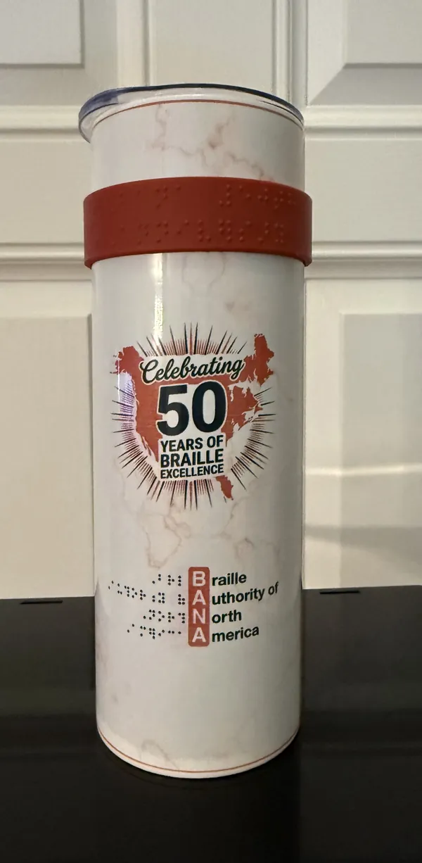 BANA 50th Anniversary braille tumbler — white marble finish with a red resin band carrying raised tactile braille.